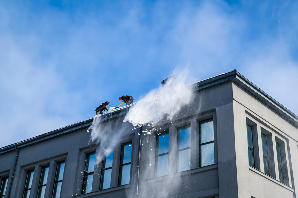 Crew cleaning building roof from snow with shovels