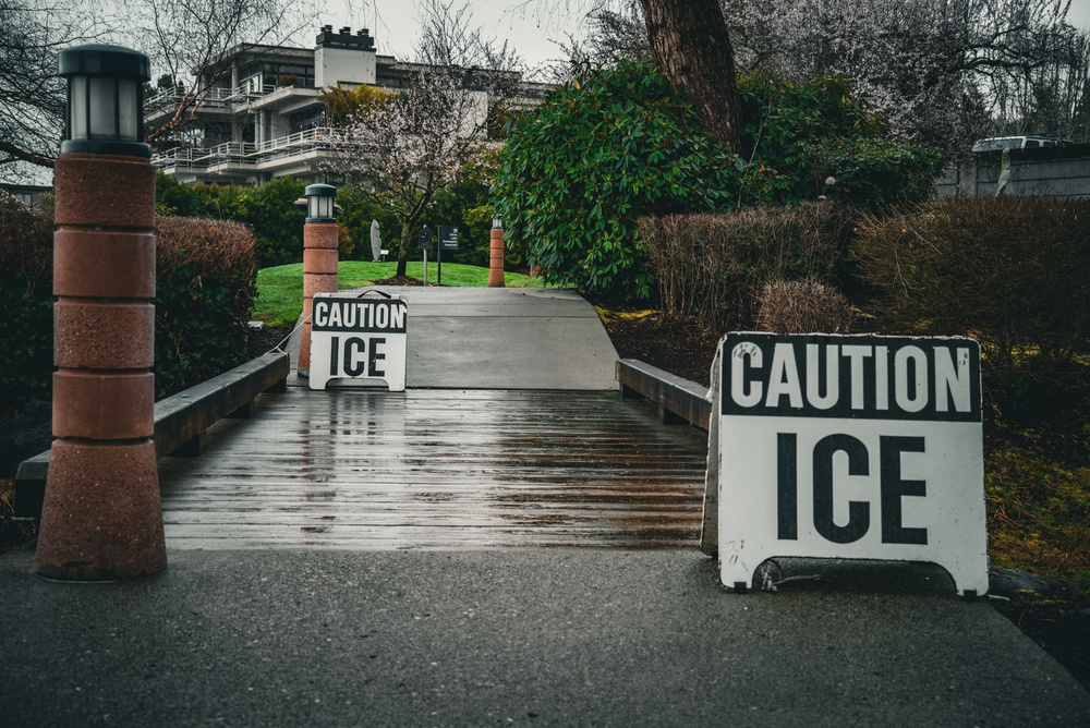 Two caution ice signs placed on wet wooden walkway