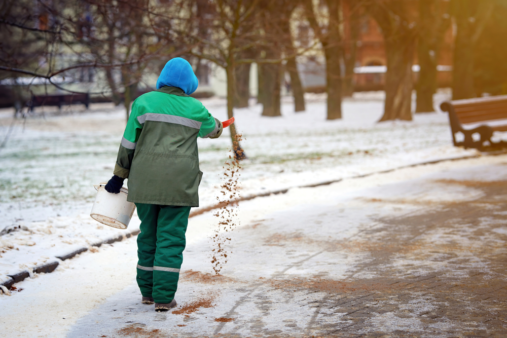 Worker spreading de-icing sand and salt on road